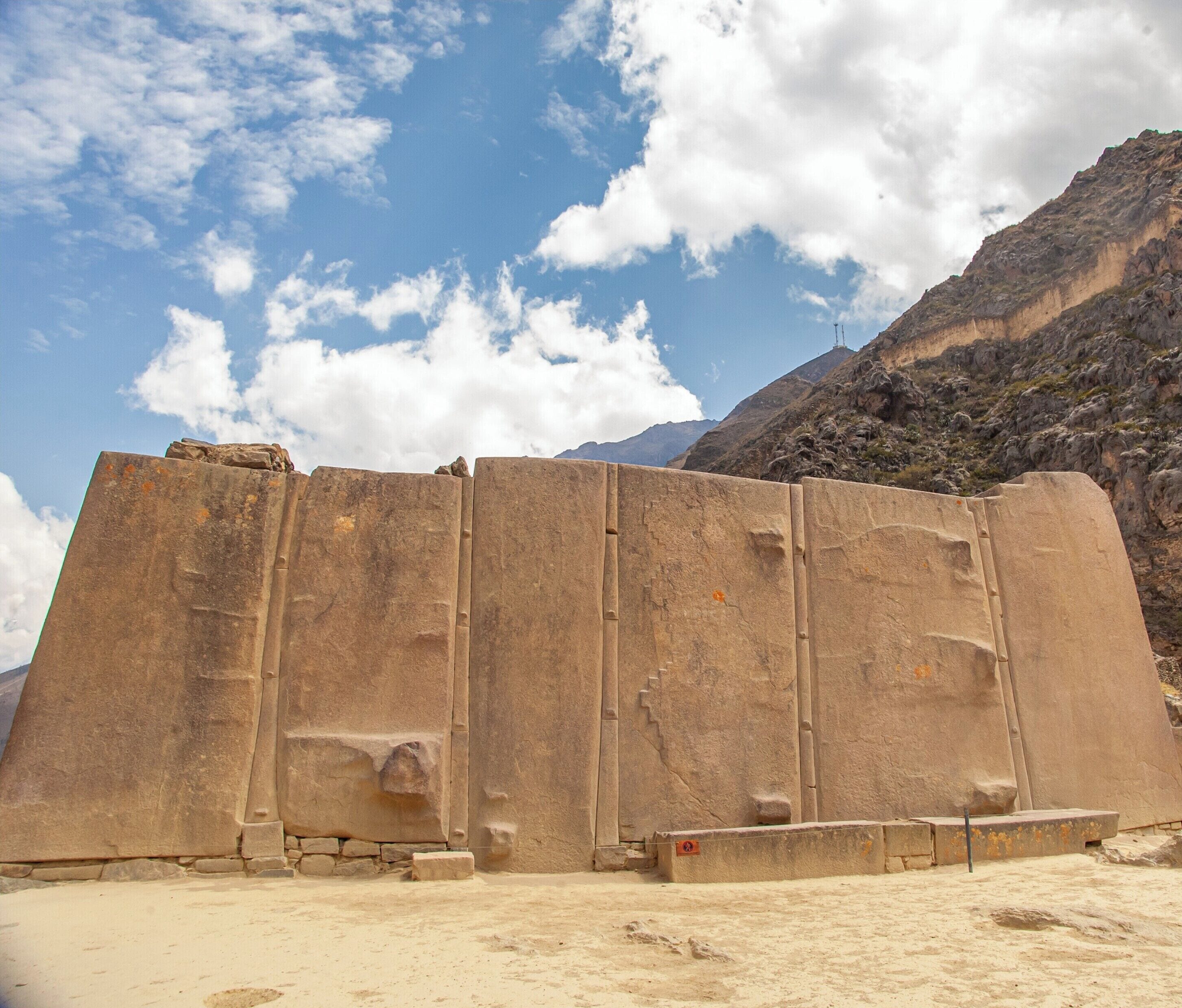 Una gran estructura de piedra con una parte superior plana, posiblemente un monumento o muro, con montañas al fondo.