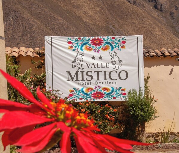 Schild für das Valle Mistico Hotel Boutique mit dekorativen floralen Mustern und zwei Schweinebildern.