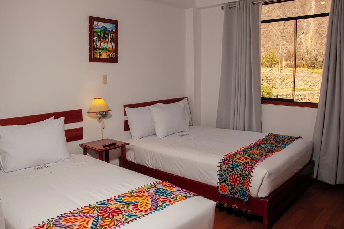 Een hotelkamer met twee bedden, een nachtkastje, een lamp, een schilderij aan de muur en een raam met gordijnen.