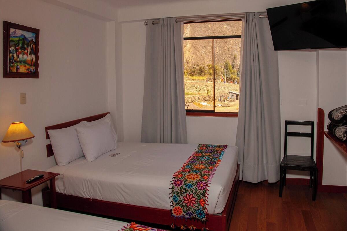 Een hotelkamer met twee bedden, een televisie, een schilderij en een raam met gordijnen.