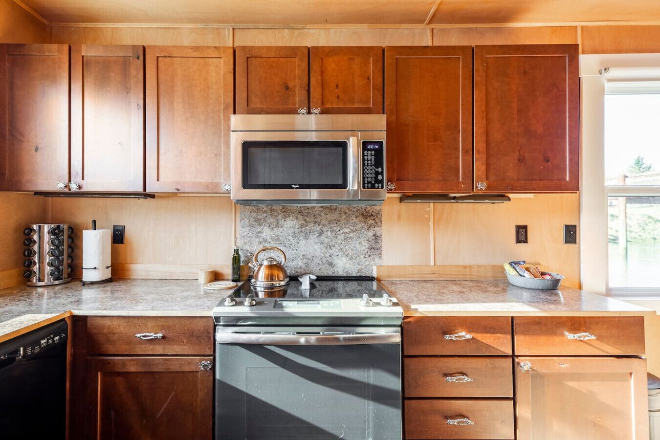 A kitchen with wooden cabinets, a stainless steel microwave, a kettle, and a dishwasher.