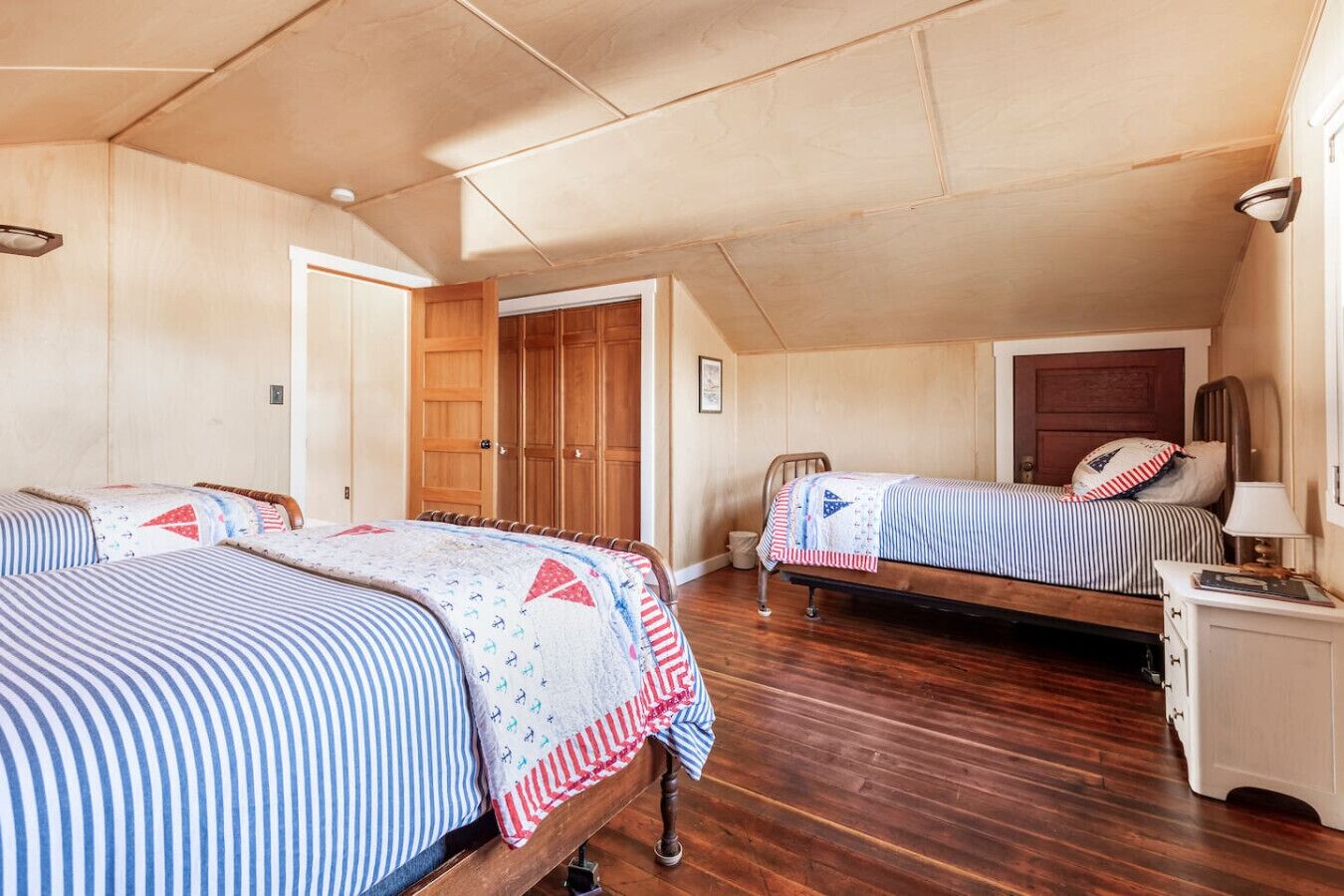 A bedroom with two beds, wooden flooring, and a wooden wardrobe.