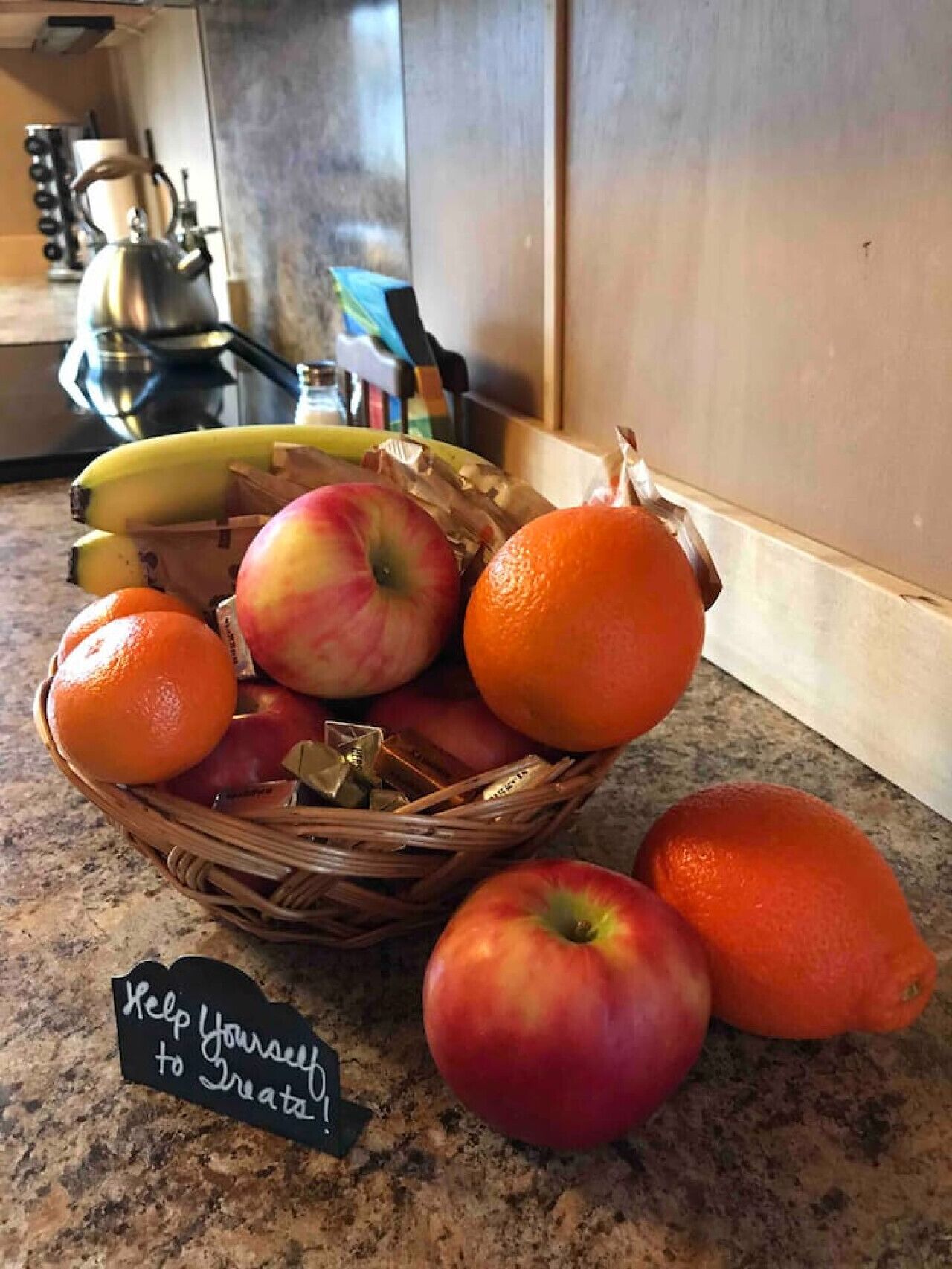 Een keukentafel met een rieten mand vol appels, sinaasappels en bananen.