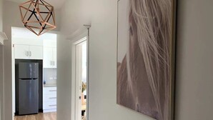 A hallway with a modern kitchen in the background, a geometric pendant light, and a framed abstract painting. - Renovated Character Home (Invermay)