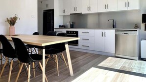 A modern kitchen with white cabinets, a wooden dining table, and black chairs. - Renovated Character Home (Invermay)