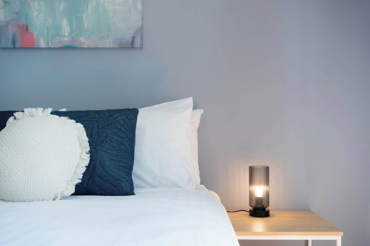 A neatly made bed with white and blue bedding, a bedside lamp, and a painting on the wall.