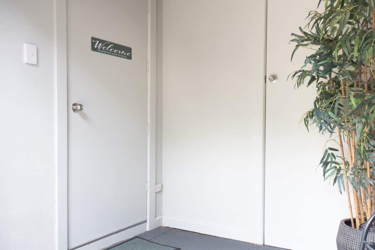 Una puerta con un letrero de 'Welcome', un felpudo y una planta en maceta.