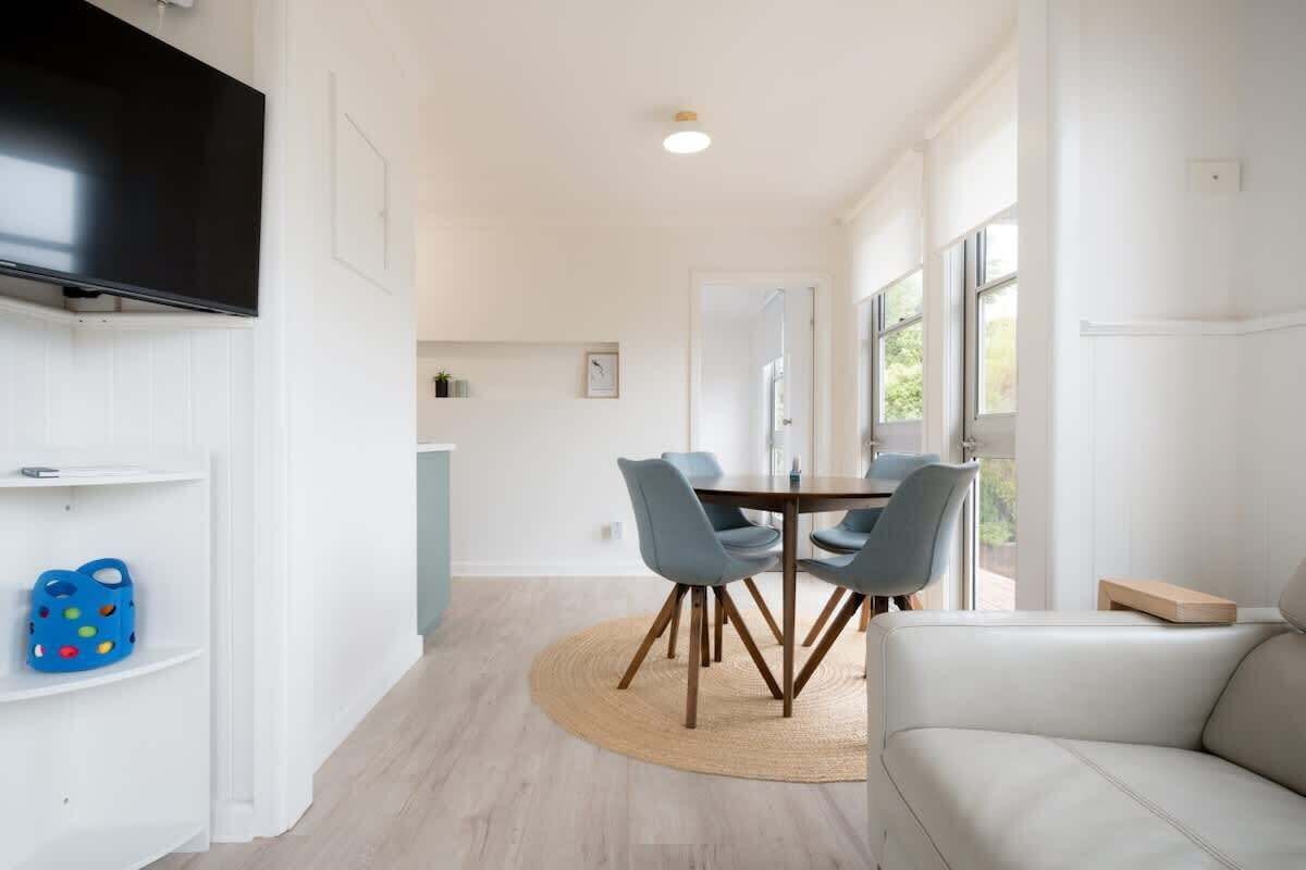 A modern dining area with a round table, chairs, and a flat-screen TV mounted on the wall.