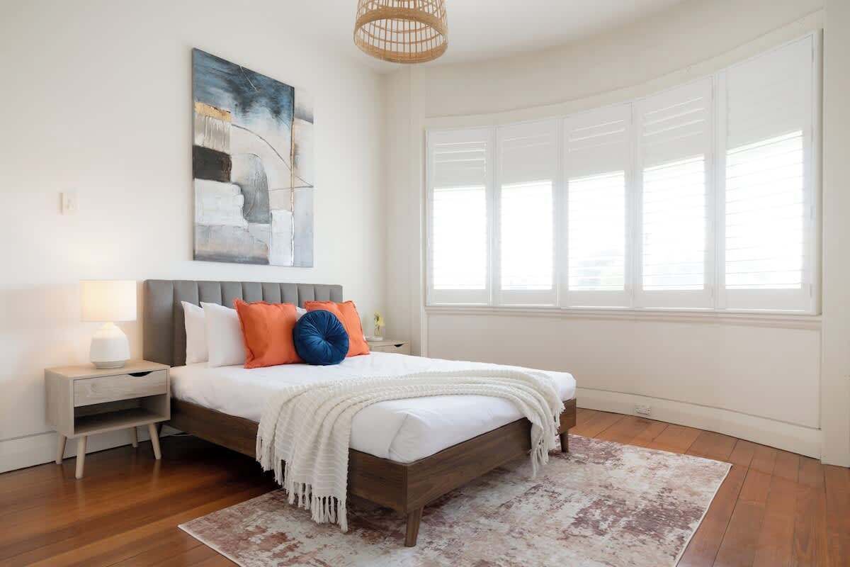 Een slaapkamer met een bed, nachtkastje, bedlamp en een groot raam.
