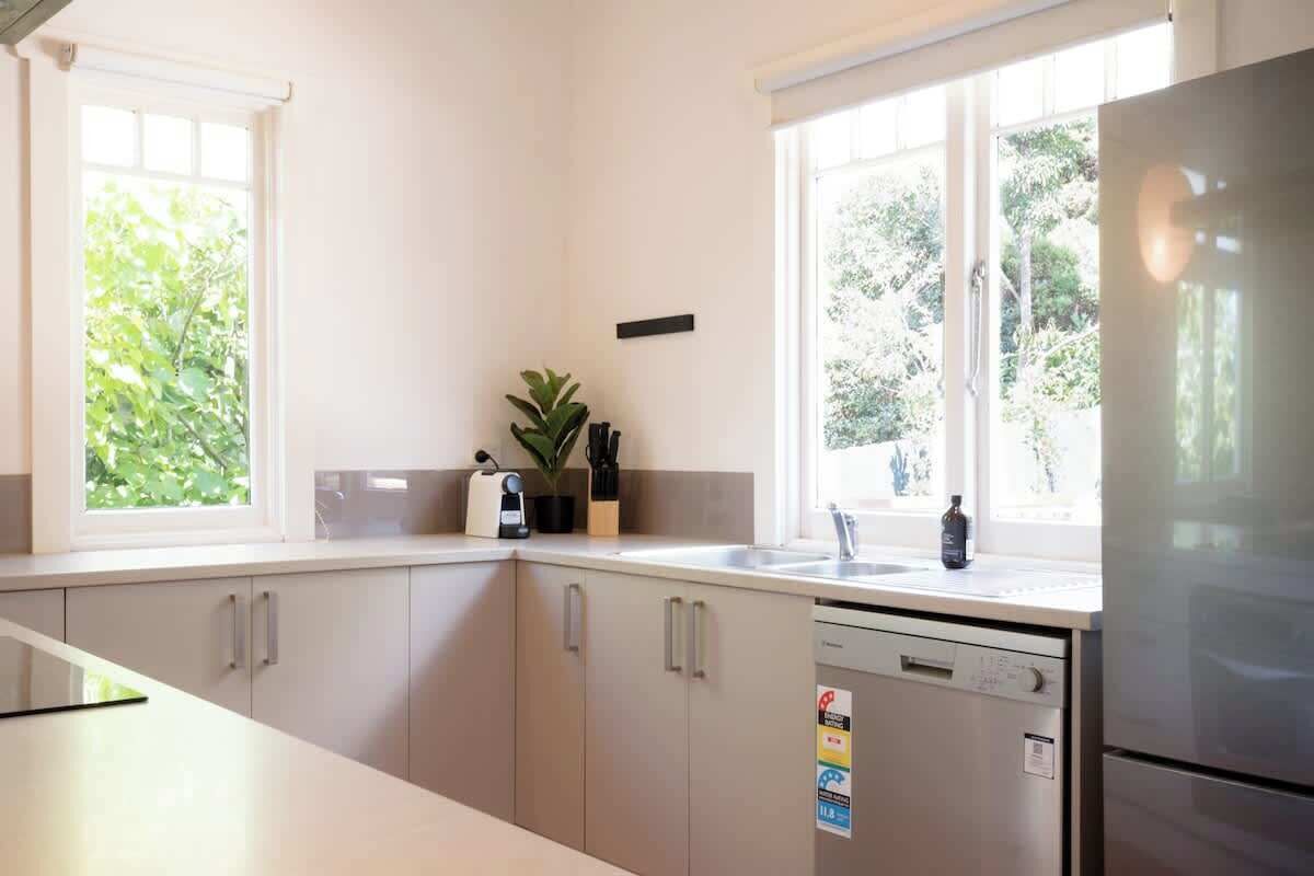 A kitchen with white cabinets, a stainless steel refrigerator, and a window with a view of greenery.