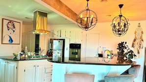 A modern kitchen with white cabinets, a central island with bar stools, and pendant lighting. - Charming bungalow house in Sherman Oaks w/ pool table, fire pit, hot tub & piano (Los Angeles)