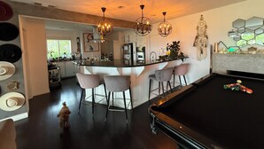 A modern kitchen with a central island, bar stools, and a pool table. - Charming bungalow house in Sherman Oaks w/ pool table, fire pit, hot tub & piano (Los Angeles)