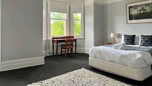 Une chambre dotée d’un grand lit, d’un bureau et d’une chaise, et d’une fenêtre laissant entrer la lumière naturelle.