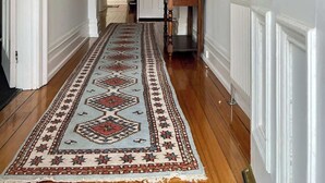 Un couloir avec un tapis à motifs, un lustre et une porte avec un radiateur.