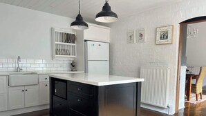 Une cuisine avec des meubles blancs, un îlot central noir et des luminaires suspendus.