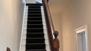 Una scala con balaustre in legno e un corrimano rivestito di tappeto nero, che conduce a una stanza con una porta bianca.