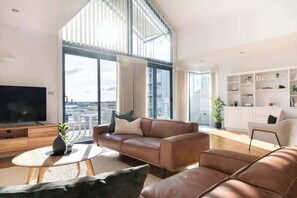 A modern living room with a large TV, leather sofa, and a view of the city. - Riverview Waterfront Stay! (Launceston)