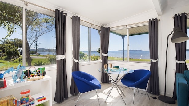 A room with a view of the sea, two blue chairs, a table with a book, and a lamp. - Waterfront Cottage - direct waterfront access, boat-friendly block, firepit, water views (Swan Bay)