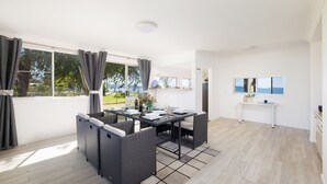 A modern dining area with a table set for two, a view of the outdoors, and a minimalist interior design. - Waterfront Cottage - direct waterfront access, boat-friendly block, firepit, water views (Swan Bay)