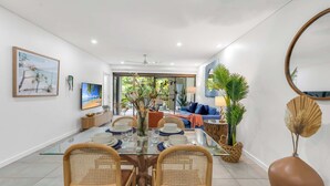 A modern dining area with a glass table, wicker chairs, and a view into the living room. - Temple Breeze - Swim Out Apartment (Port Douglas)