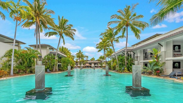 A resort pool with clear water, surrounded by palm trees and modern buildings. - Temple Breeze - Swim Out Apartment (Port Douglas)