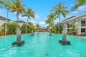 Ein Hotelpool mit klarem Wasser, umgeben von Palmen und modernen Gebäuden.