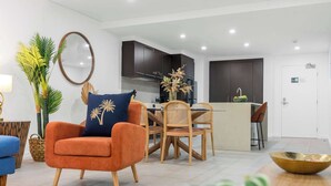 A modern living room with a sofa, chairs, a coffee table, and a kitchen area with cabinets and a dining table. - Temple Breeze - Swim Out Apartment (Port Douglas)