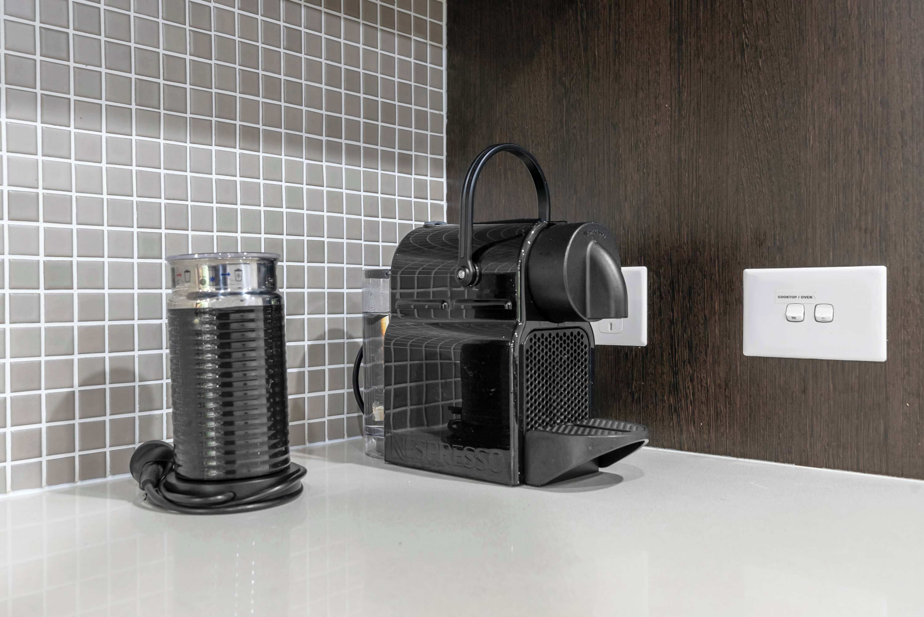 A Nespresso coffee machine on a white countertop with a tiled backsplash and a wooden panel wall.