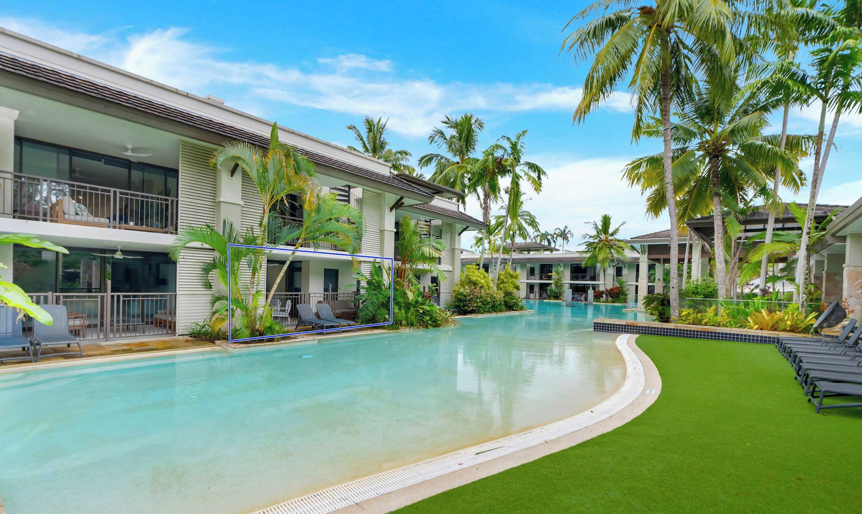 A resort pool area with a clear blue pool, lounge chairs, and palm trees.