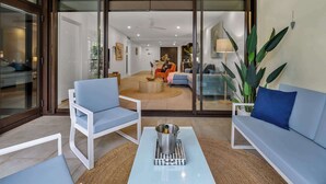 Ein modernes Wohnzimmer mit Glastür zum Balkon, einem weißen Sofa, einem blauen Sessel und einem Couchtisch mit einer Flasche.
