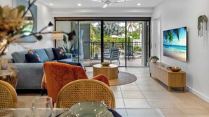 Ein modernes Wohnzimmer mit Sofa, Esstisch und Stühlen, einem Fernseher und einem Balkon mit Gartenmöbeln.