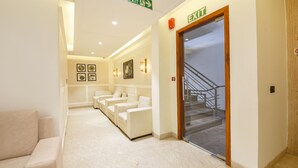 Un hall d’hôtel comprenant un comptoir d’accueil, un escalier et un panneau indiquant la sortie de secours en cas d’incendie.