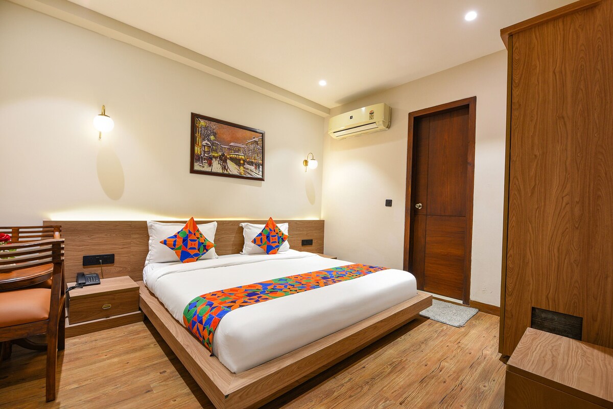 A hotel room with a large bed, a desk with a chair, a desk lamp, a wall-mounted phone, and an air conditioning unit.
