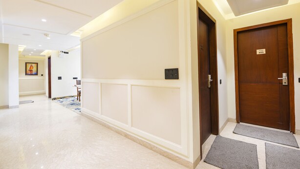 Un couloir d’hôtel avec une porte en bois portant l’inscription « Suite 405 », un espace de réception et un sol recouvert de moquette.