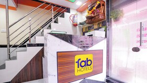 A hotel reception area with a marble staircase, a fire extinguisher, and a decorative shelf with flowers. - Fabexpress Raj Palace (Mumbai)