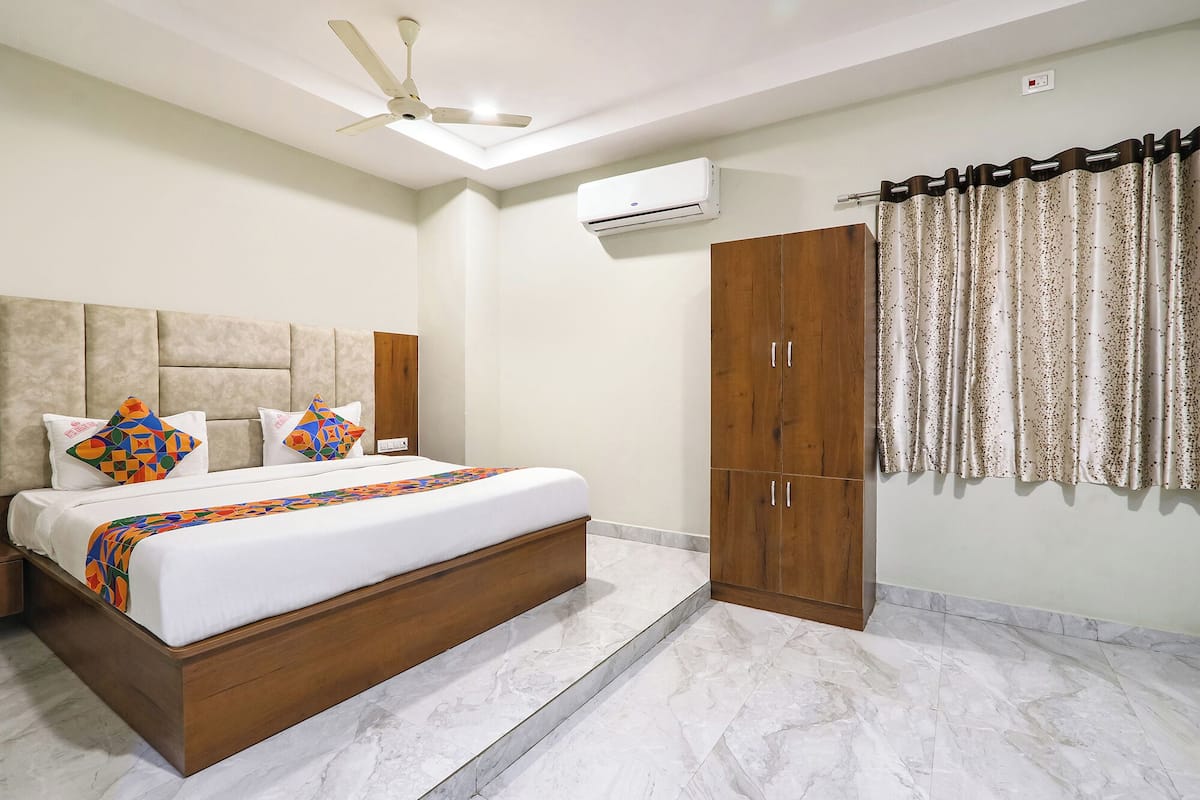 A hotel room with a bed, a wardrobe, a ceiling fan, an air conditioning unit, and a window with curtains.