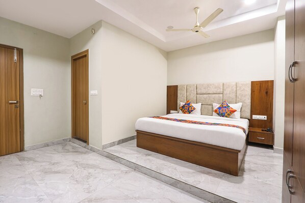 Une chambre d’hôtel avec un lit, un ventilateur de plafond, une armoire en bois et un sol en marbre.