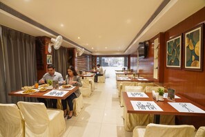 A dining area with tables, chairs, and a view of the street outside. - FabHotel Pleasure Inn - Nr. DB Mall (Bhopal)