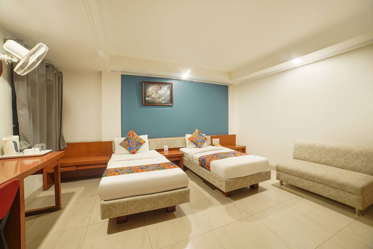 A hotel room with two beds, a sofa, a desk with a chair, and a ceiling fan.