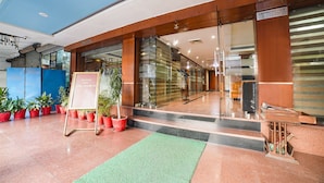 L’entrée d’un hôtel, avec un comptoir d’accueil, un tapis vert et des plantes en pot.