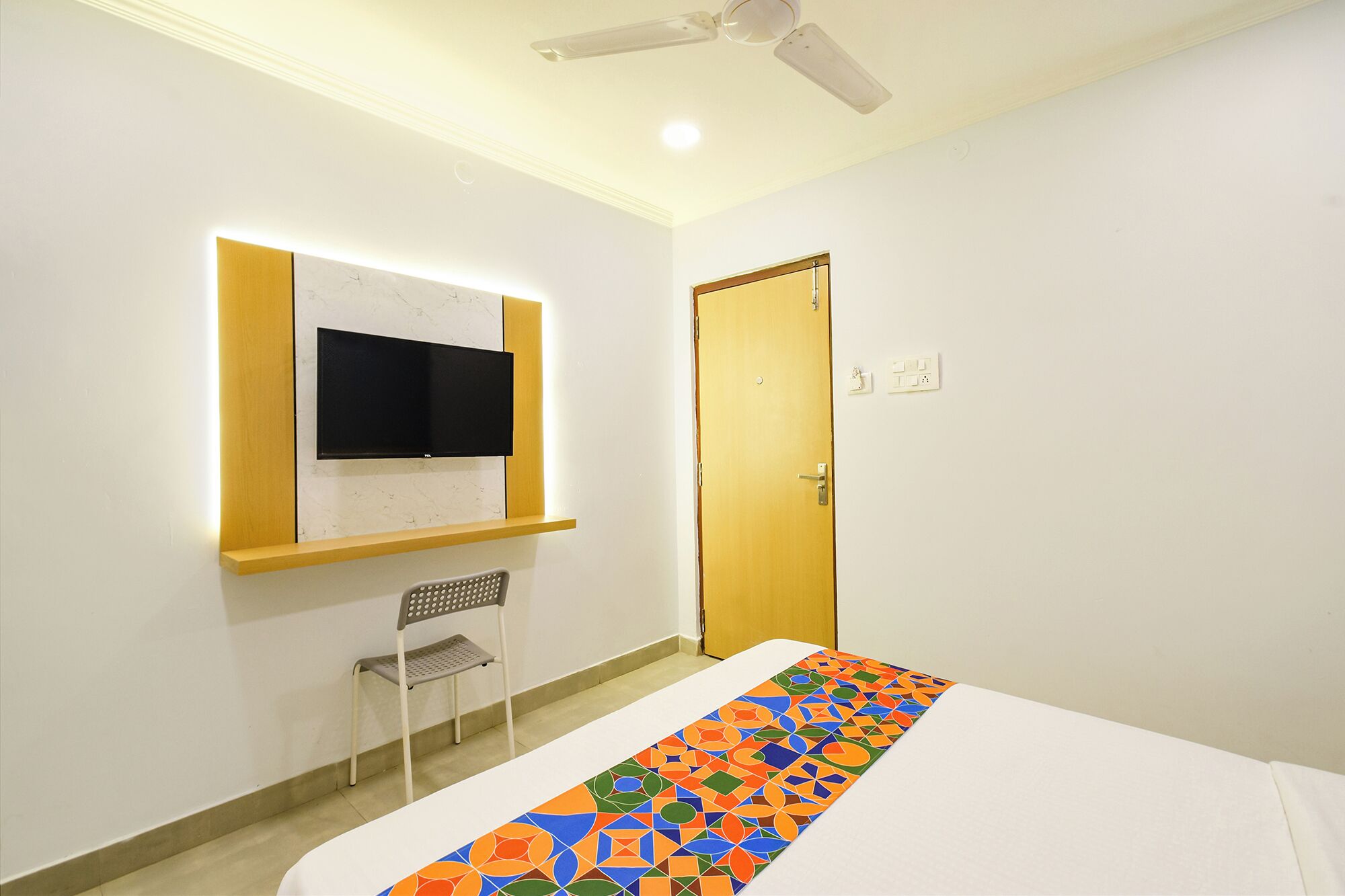 A hotel room with a bed, a television mounted on a wall, a chair, and a door.