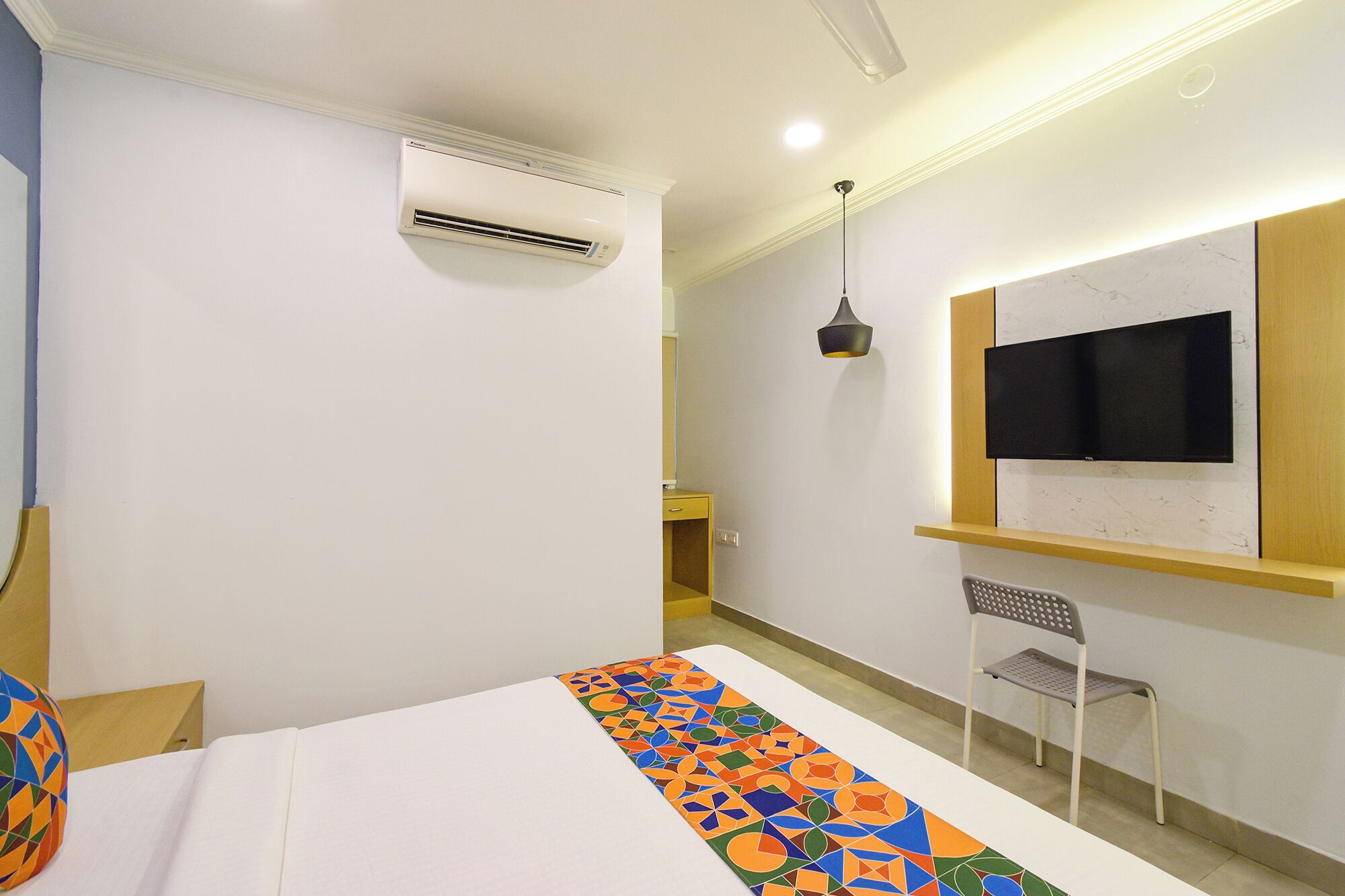 Camera d'albergo con un letto, una televisione a parete, un condizionatore d'aria, una sedia e un tappeto colorato.
