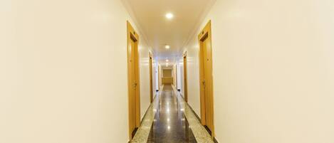 A long, narrow hotel corridor with wooden doors on both sides and a polished marble floor.