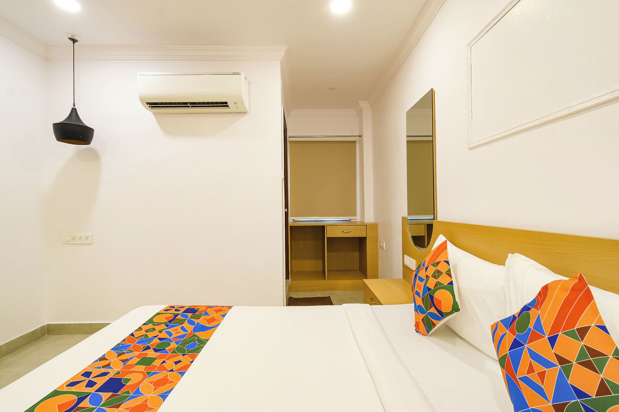A hotel room with a bed, a desk, an air conditioner, and a mirror.