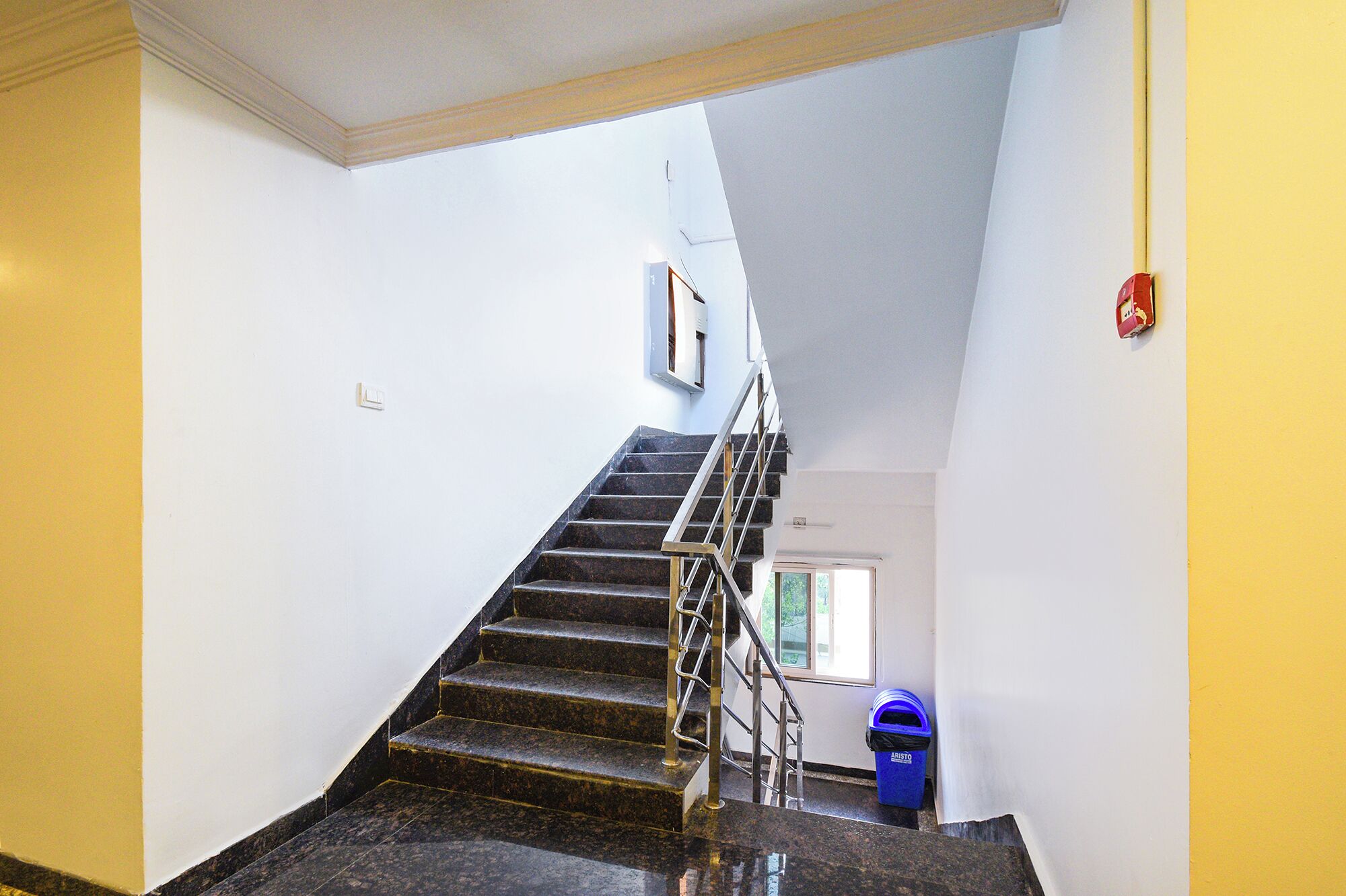 A staircase with a handrail, a blue trash bin, and a fire alarm on the wall.