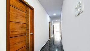 A hallway with a wooden door, white walls, and a black tiled floor. - Fabhotel Living Tree (Hyderabad)