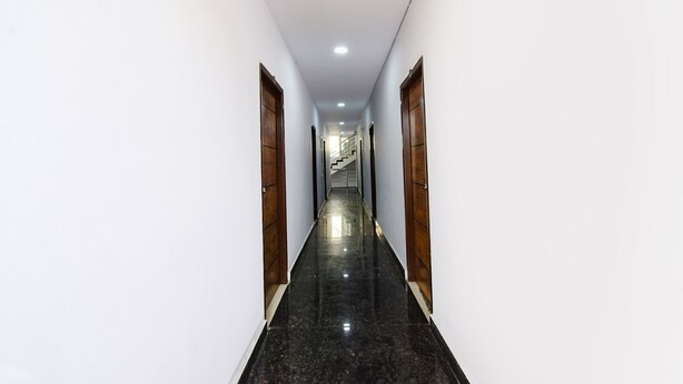 A long, narrow hallway with polished black floors and white walls, leading to a staircase at the end. - Fabhotel Living Tree (Hyderabad)