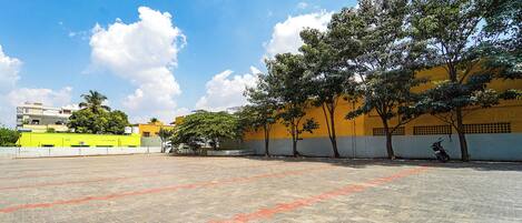 An outdoor paved area with a yellow building in the background, trees, and a parked motorcycle.