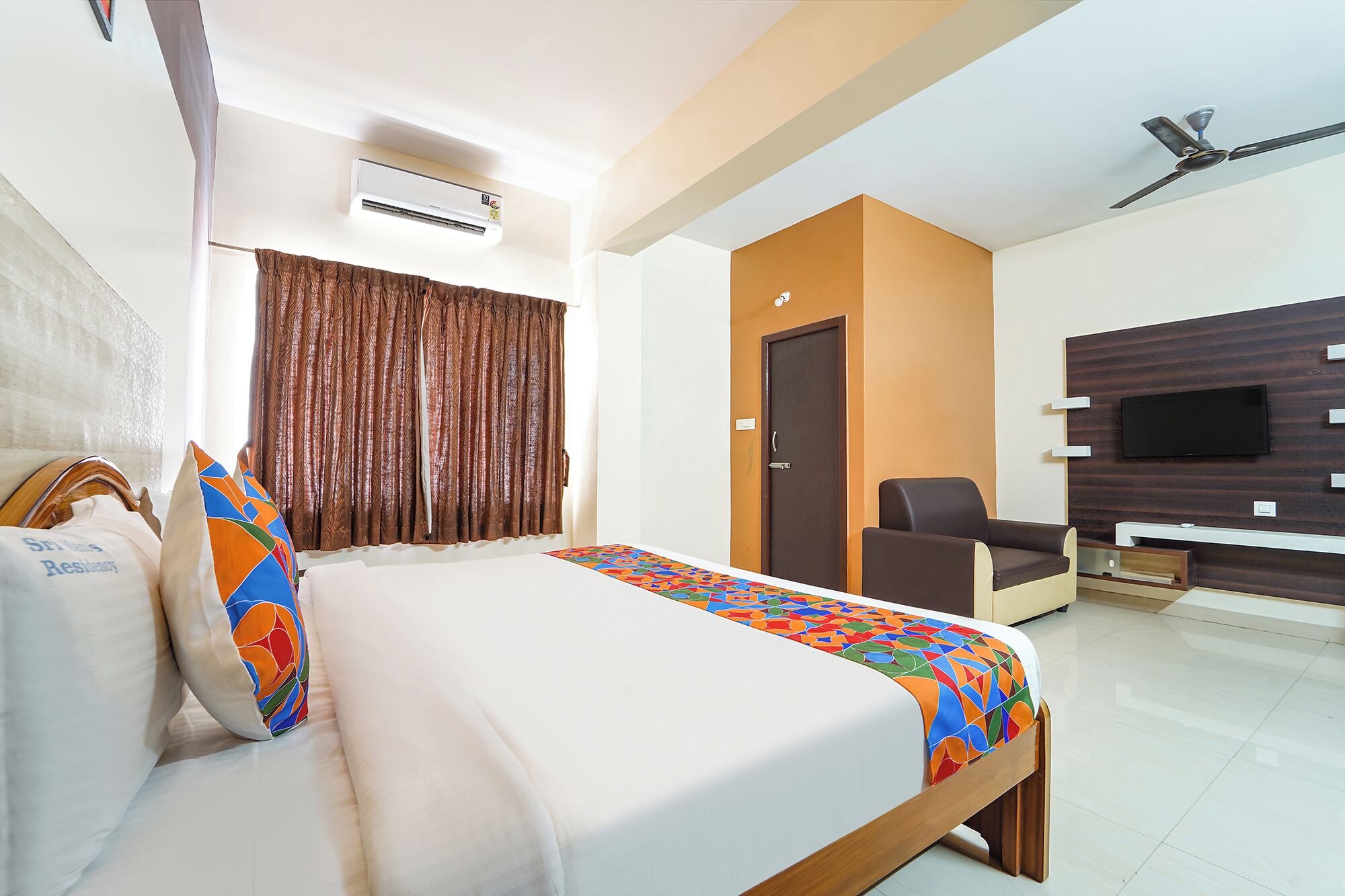 A hotel room with a bed, a chair, a TV, and an air conditioning unit.