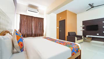 A hotel room with a bed, a chair, a TV, and an air conditioning unit.